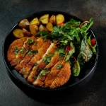 Kotlet z ziemniakami i sałatą na czarnym talerzu